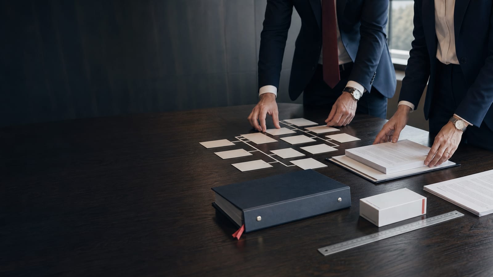 Corporate professionals arranging an organisation structure beside controlled records and neutral pharmaceutical packaging