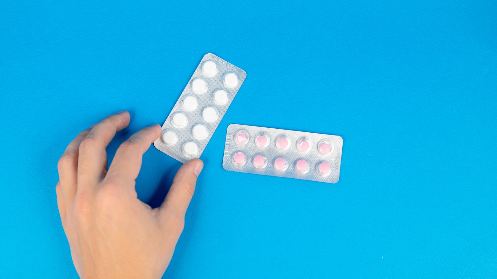 Hand holding unbranded medicine blister packs against a clean blue background