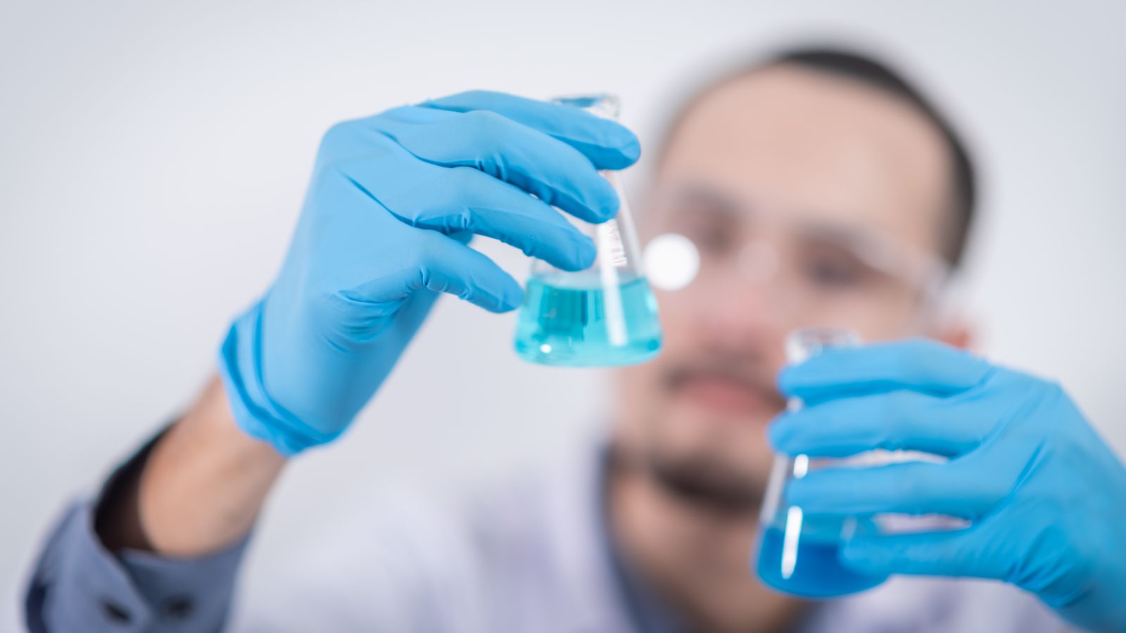 Scientist wearing gloves and safety glasses holding laboratory flasks for analysis