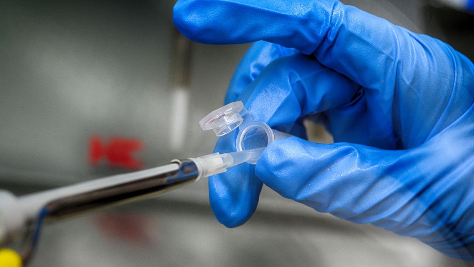 Gloved laboratory professional handling a vial with a pipette in a controlled scientific setting