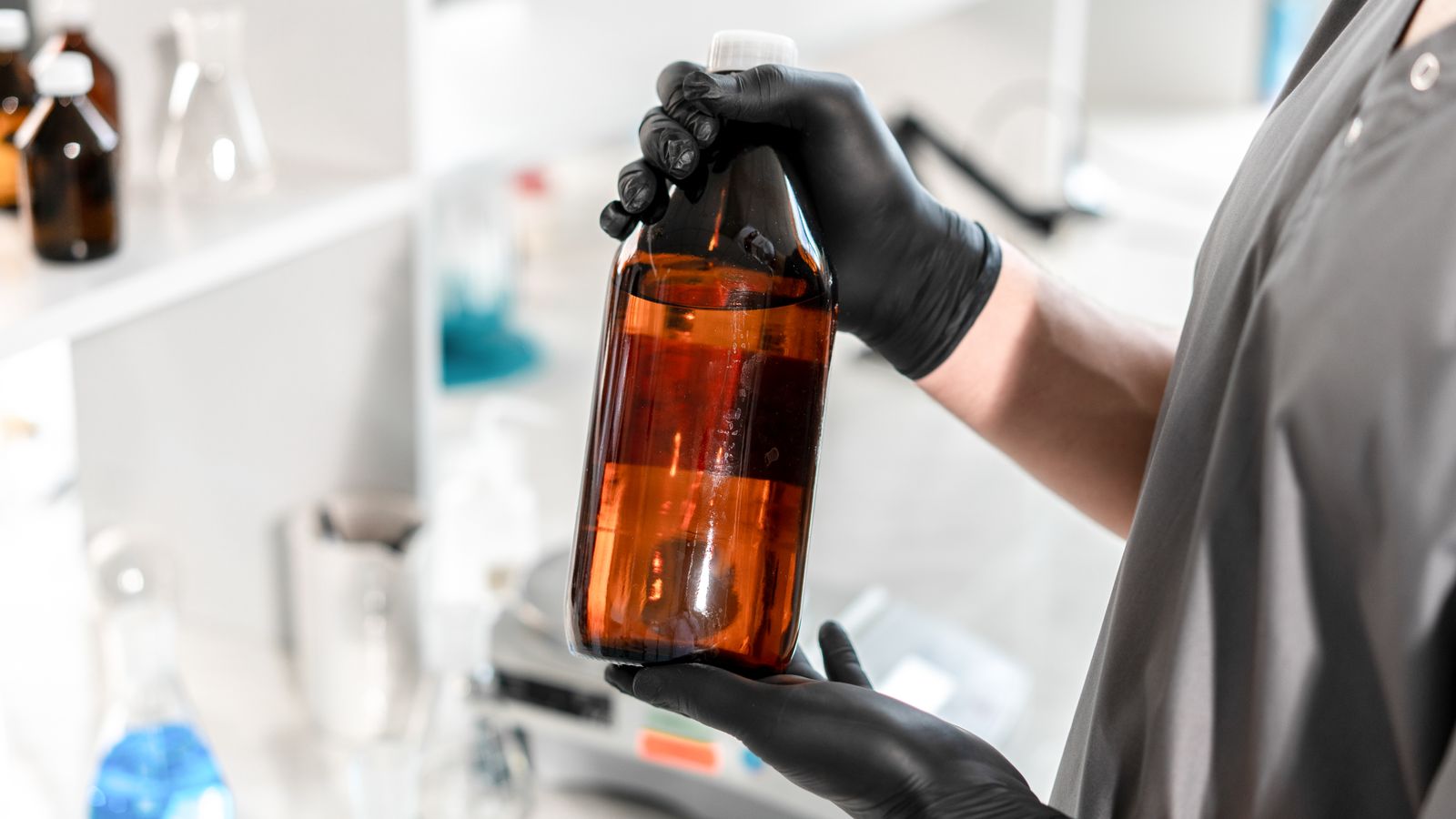 Gloved laboratory professional holding an amber glass bottle during liquid analysis